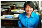 一名女学生坐在教室的课桌前，面向镜头微笑